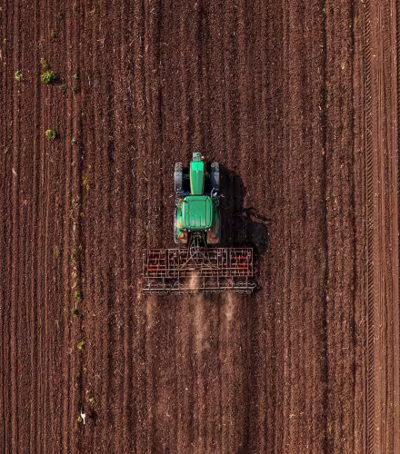 Tracteur vert équipé d'une fraise effectuant le labour avant les semailles, vue aérienne par drone
